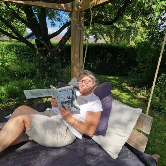 Biblioteksassistent Pia Danielsen læser i sin have 