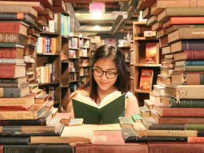 Kvinde læser i bog blandt reoler fyldt med bøger