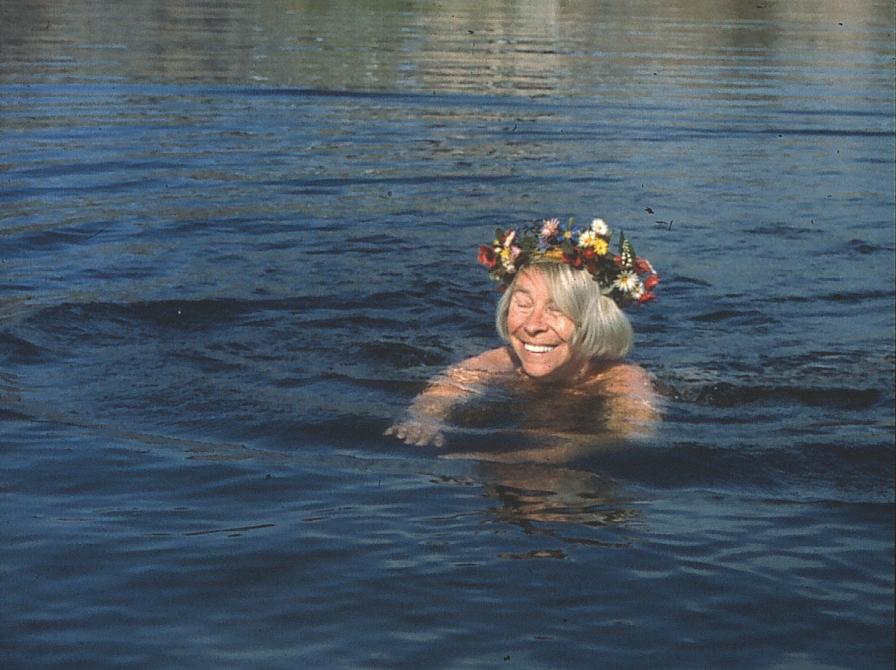 Tove Jansson svømmer i vand med blomsterkrans