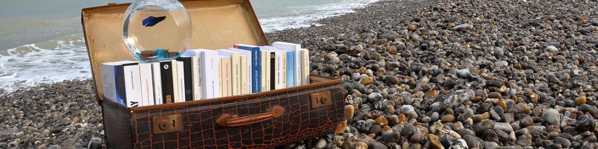 Kuffert med bøger på stranden og et fyrtårn i baggrunden